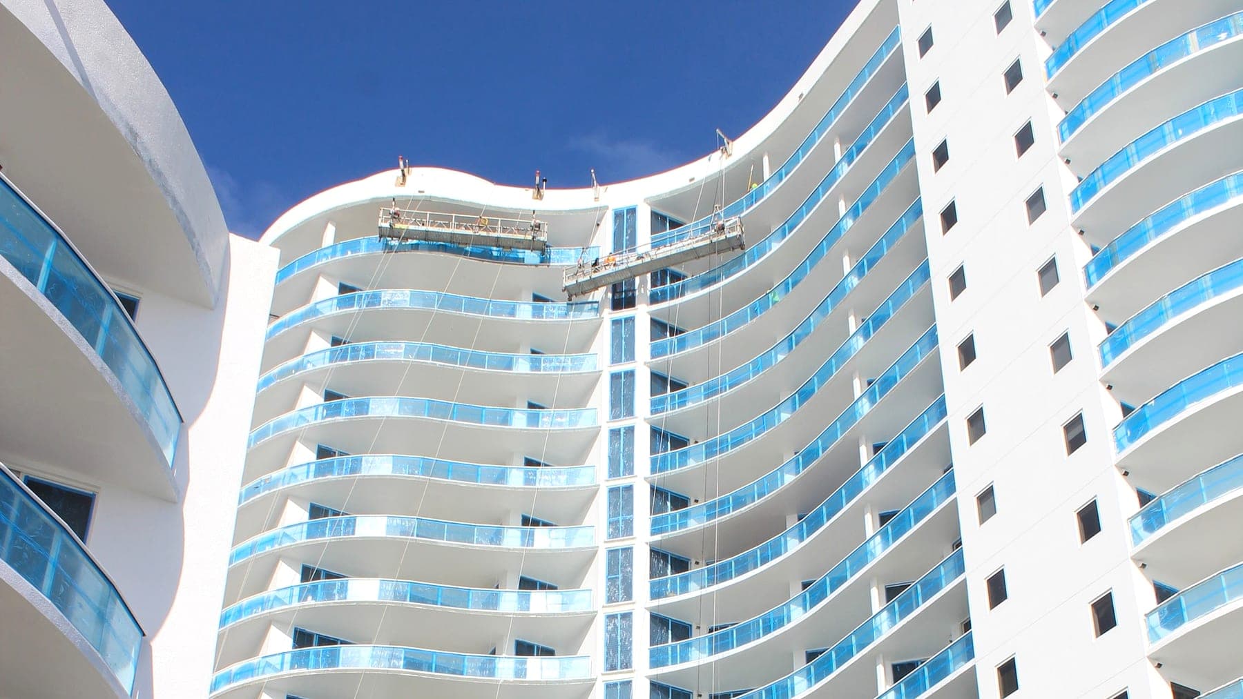 The upper floors of The Beach Front on Singer Island, with a swing stage rigged against the tower's curved balconies