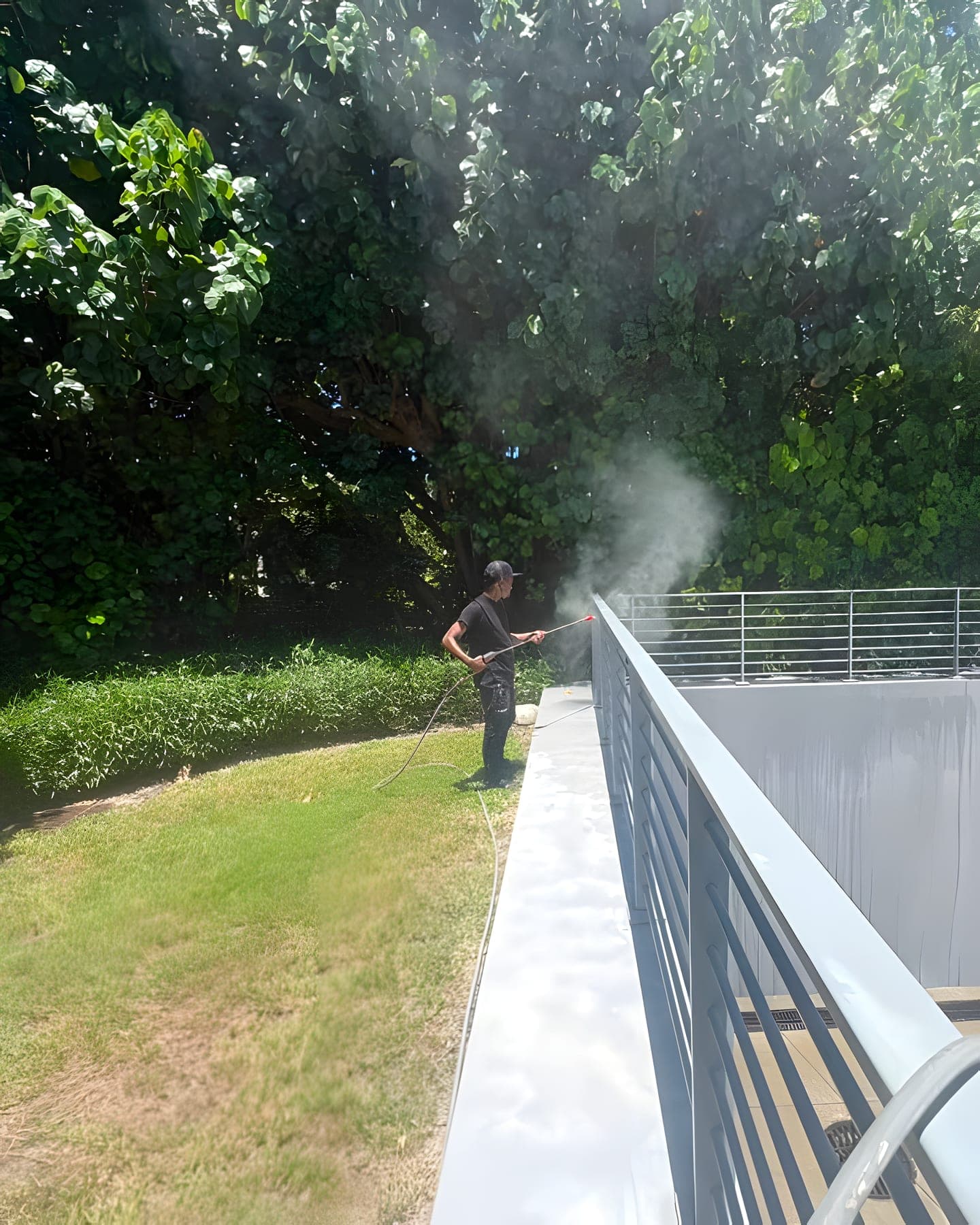 A technician soft-washing an exterior wall, with spray mist drifting along the parapet