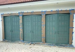 Three metal doors with their surrounds taped off in blue tape and paper before painting