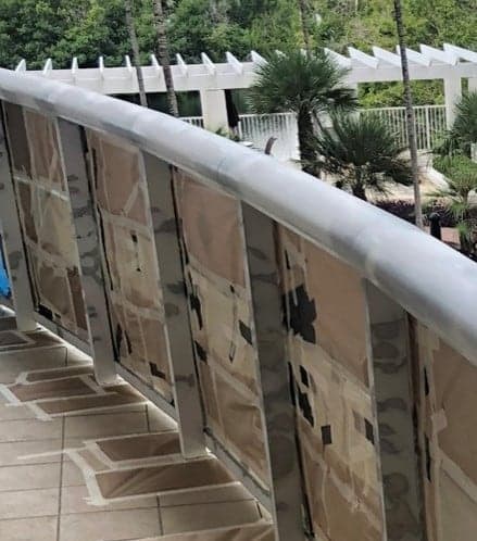 A curved balcony railing with its glass panels masked in paper before electrostatic painting
