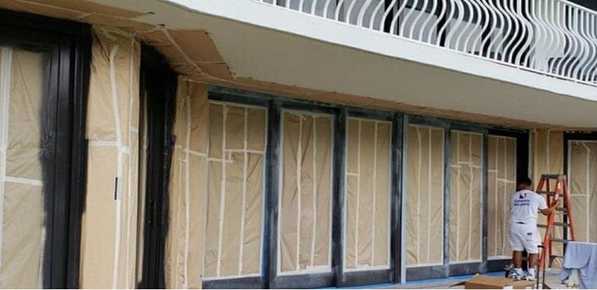 Ground-floor storefront frames with the glass covered in paper while a painter works from a ladder