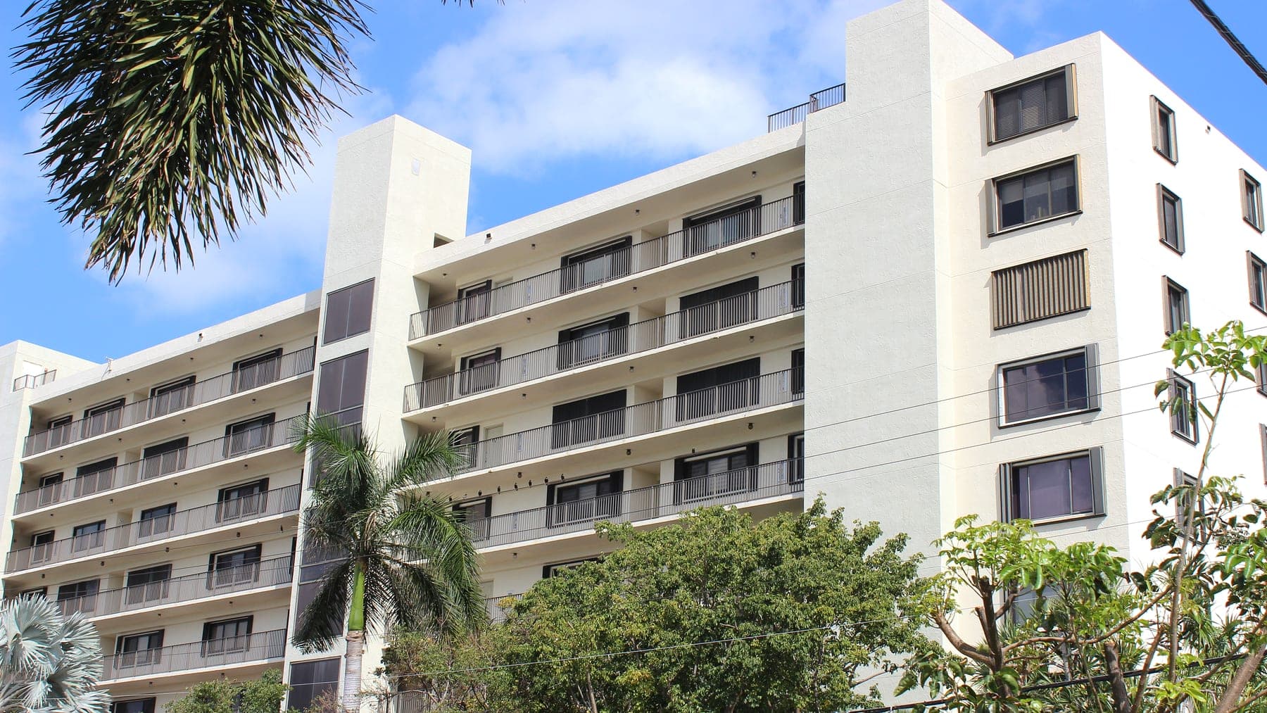 The Everglades Club building's white exterior and stacked balconies, framed by palm fronds