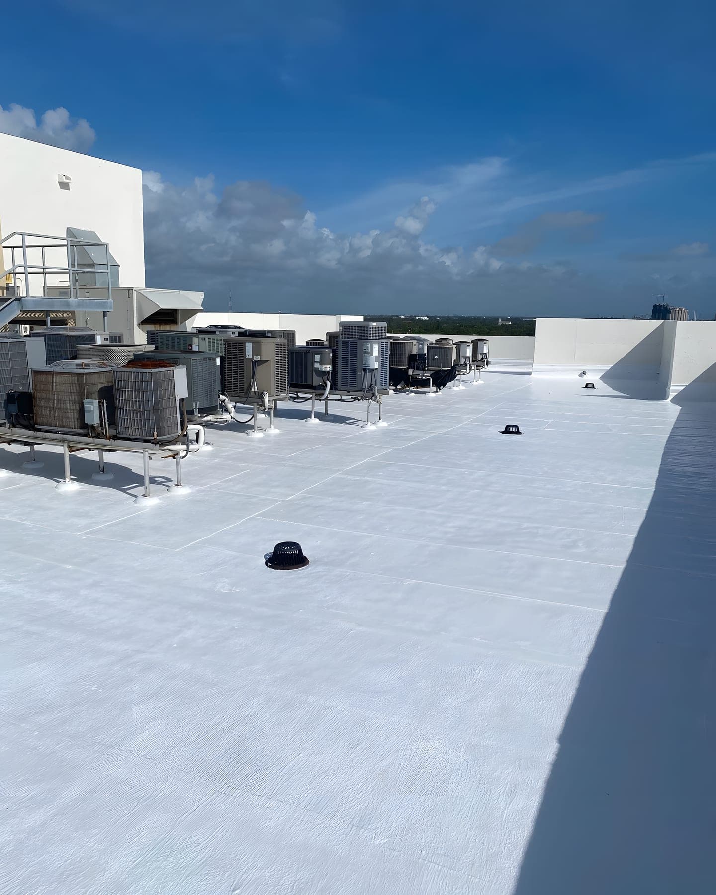 A finished white membrane roof with rooftop condenser units under a blue sky