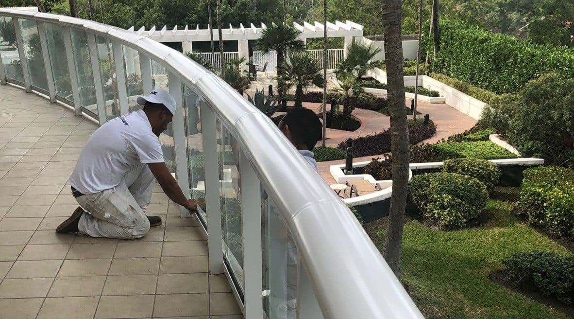 A technician applying sealant along the base of a glass balcony railing