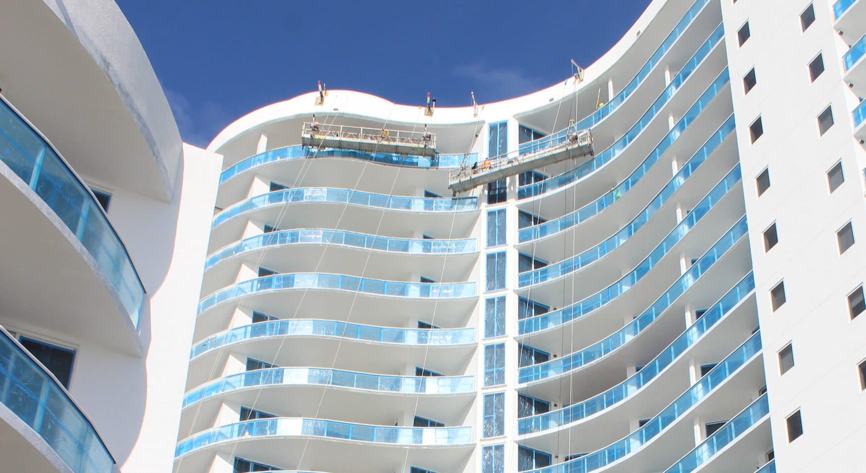 Exterior painting underway on a high-rise with glass balcony railings