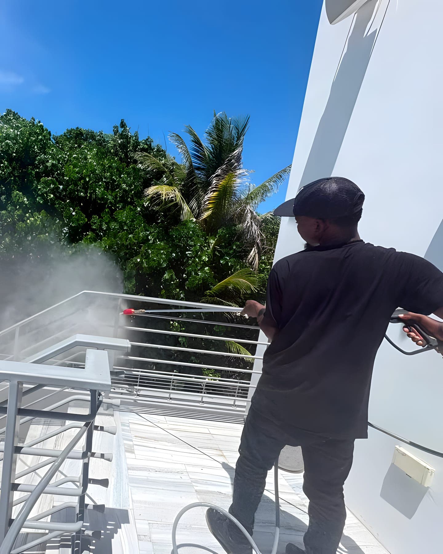 A technician rinsing a metal railing with a low-pressure wand beside lush landscaping