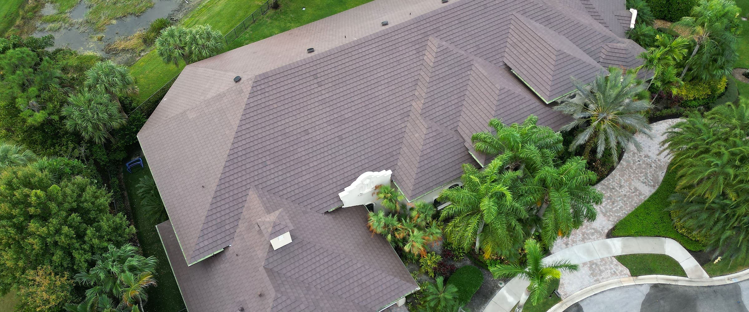 Aerial view of a single-family home and its roof among tropical landscaping