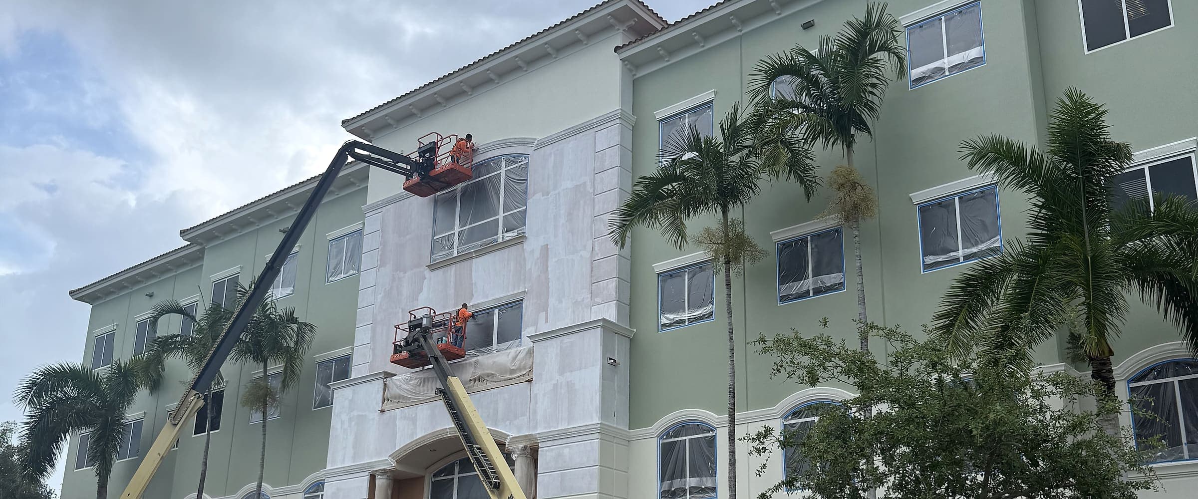 Boom lifts staged against a commercial building during exterior painting