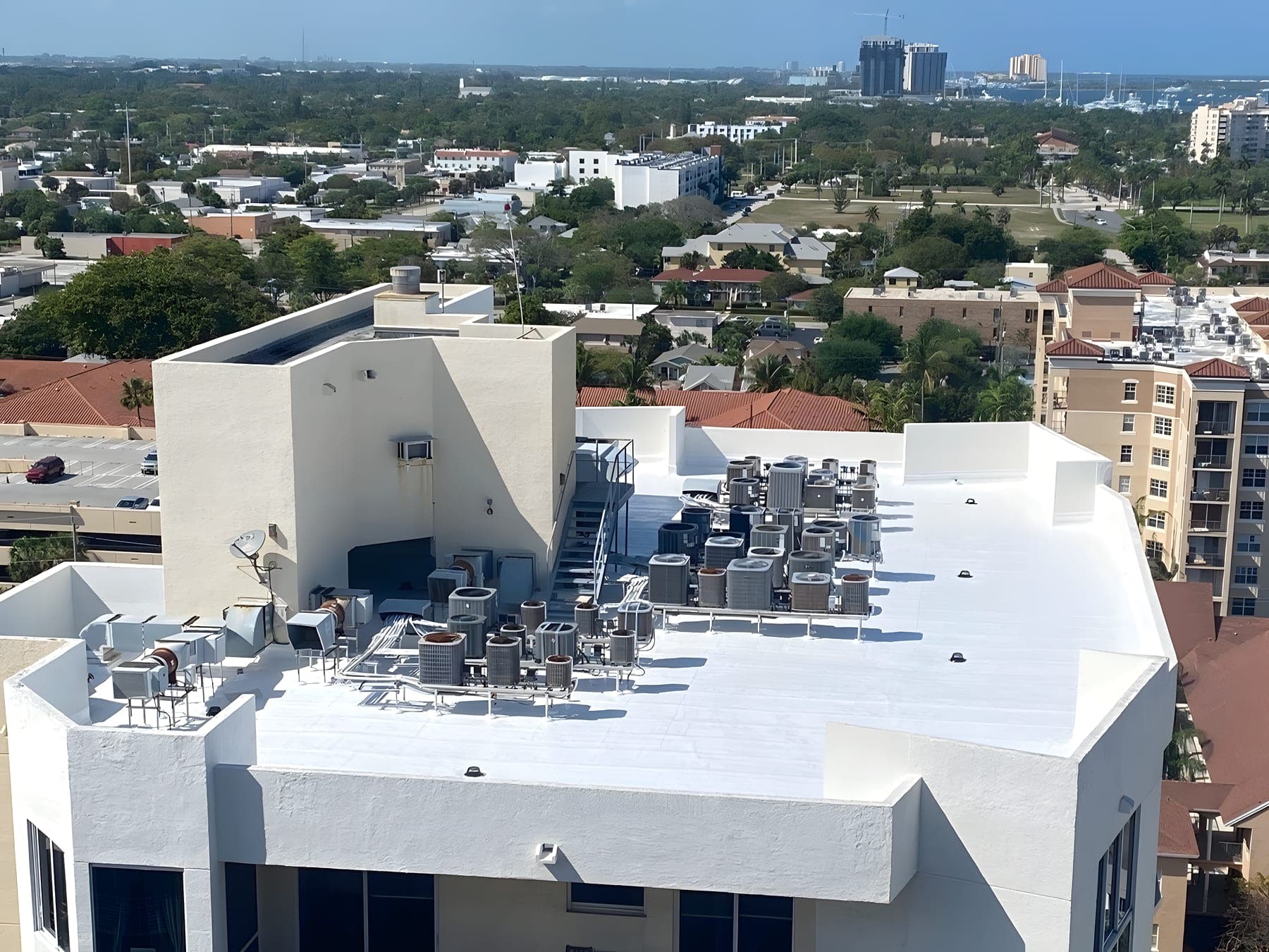 Aerial view of a white commercial roof and its rooftop mechanical units, with the city skyline beyond