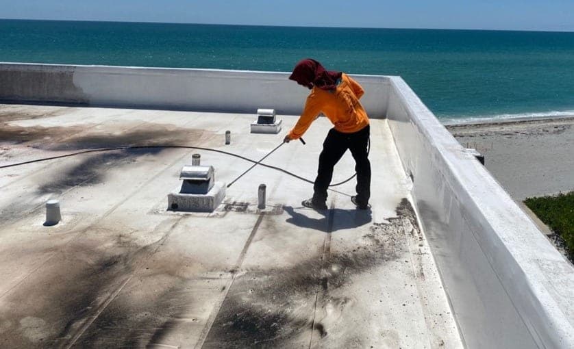 A technician washing a stained flat roof deck beside the ocean