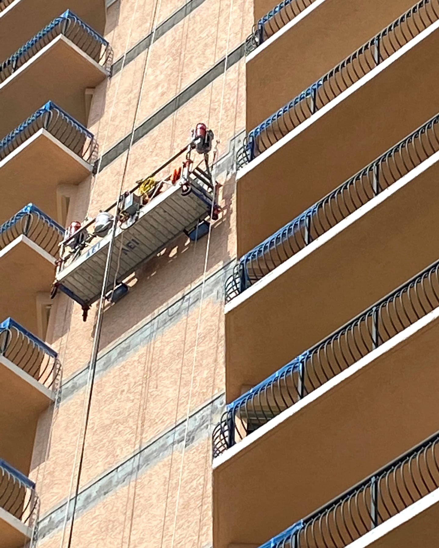 Technicians on a suspended swing stage coating the stucco wall of a high-rise