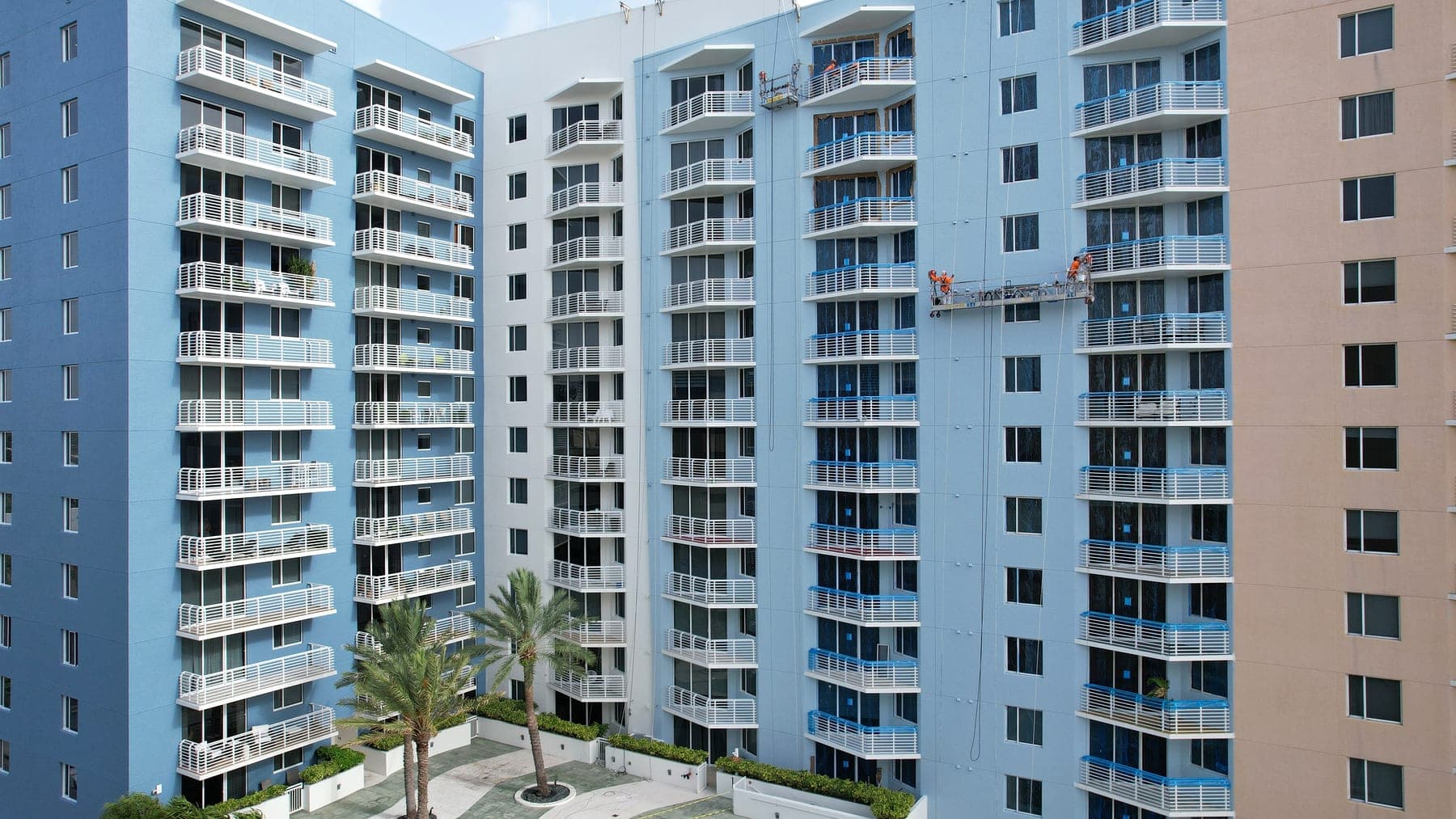 Two swing-stage crews working across neighboring condominium towers above a pool courtyard