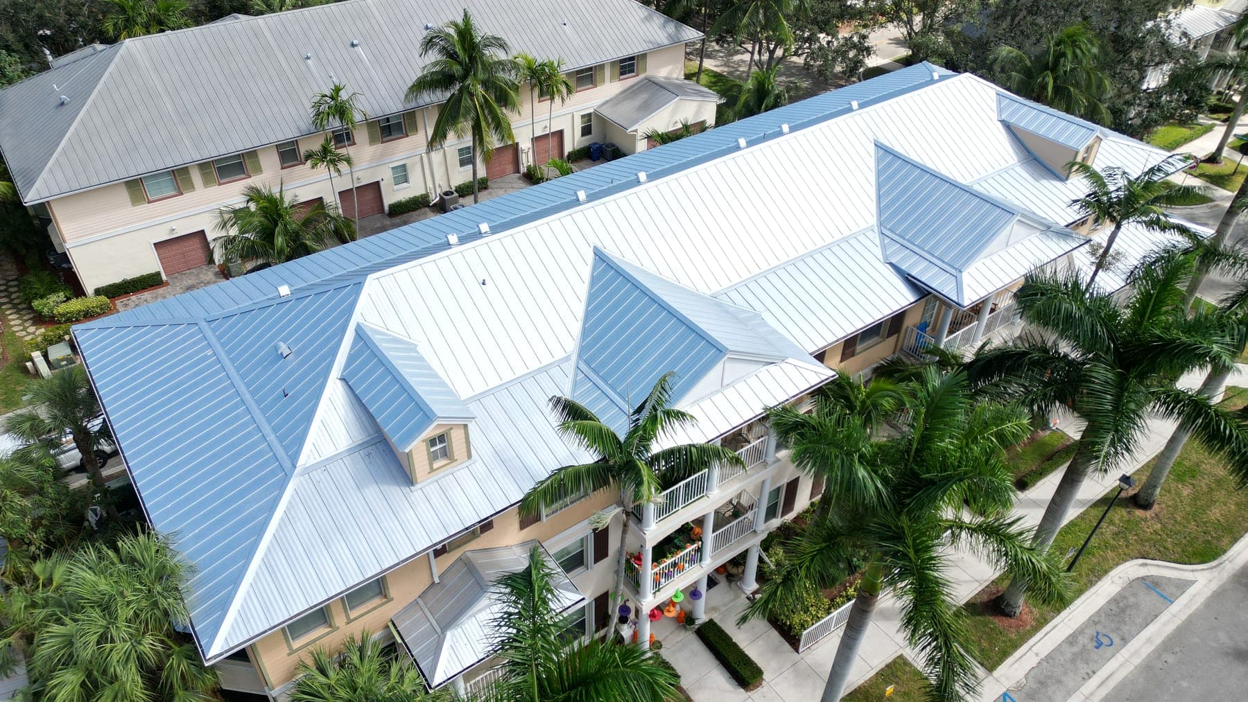 Aerial view of a multifamily townhome community with standing-seam metal roofs among palms